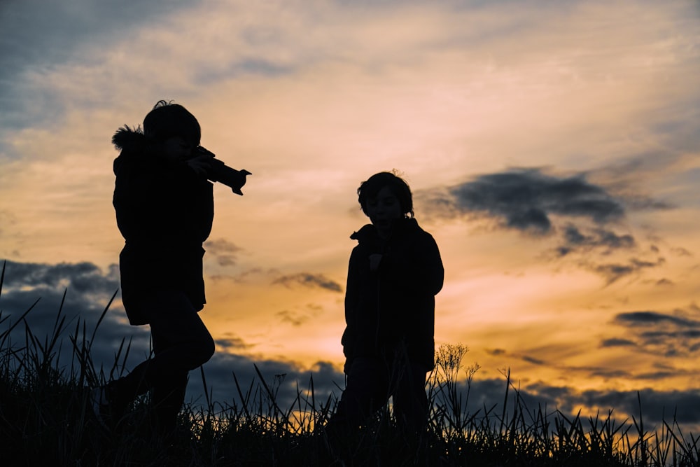 silhouette photo of two person taking a photo at grass fields