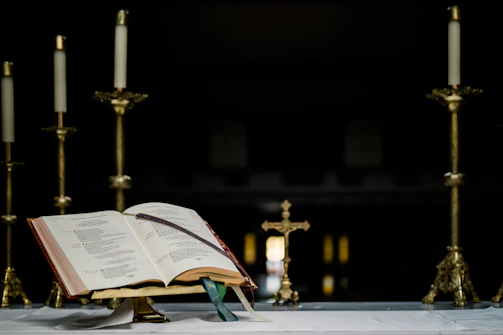 An ancient Bible open on a wooden altar with soft candlelight.