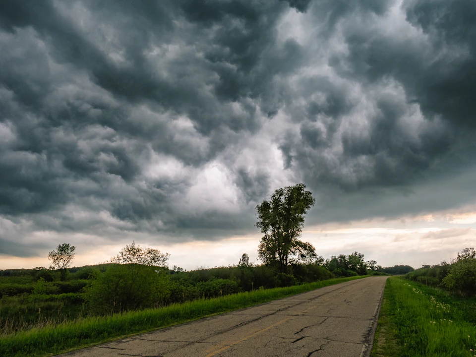 Rural landscape with empty two-lane road under dark and rainy sky with trees nearby