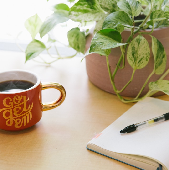 black retractable pen on opened book beside red and white go get'em-printed coffee cup