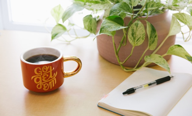 black retractable pen on opened book beside red and white go get'em-printed coffee cup