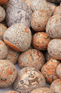 Intricately designed gourds featuring detailed carvings and paintings with motifs of animals, geometric patterns, and abstract shapes. The artwork displays a variety of sizes and colors, primarily featuring earthy tones.