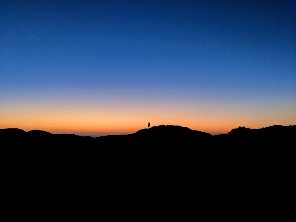 silhouette of person on mountain under clear blue sky