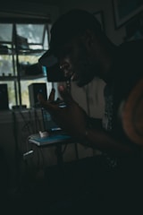 A shadowy figure working intently on futuristic tech in a dimly lit room.