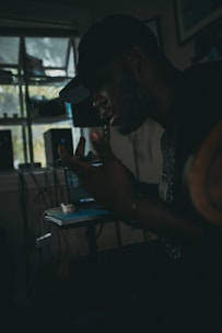 Shadowed figure in a dimly lit room analyzing network maps on multiple monitors.