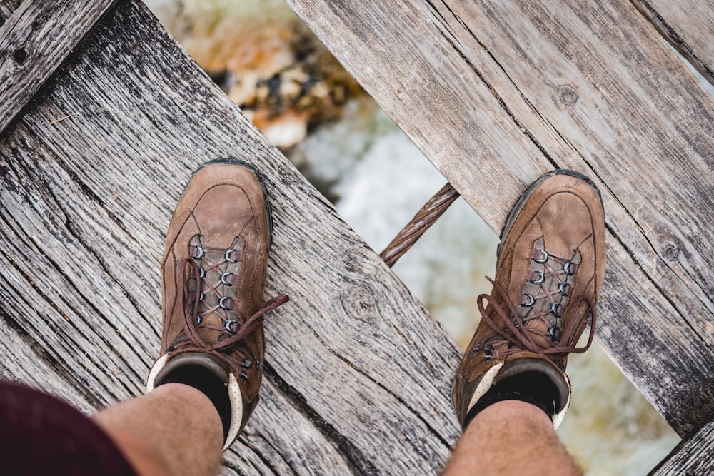 persona que lleva un par de zapatos marrones en el puente de madera debajo del río