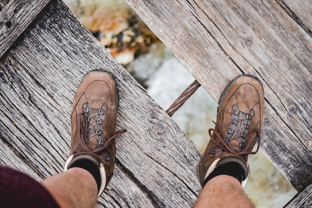 person wearing pair of brown shoes on wooden bridge under of river