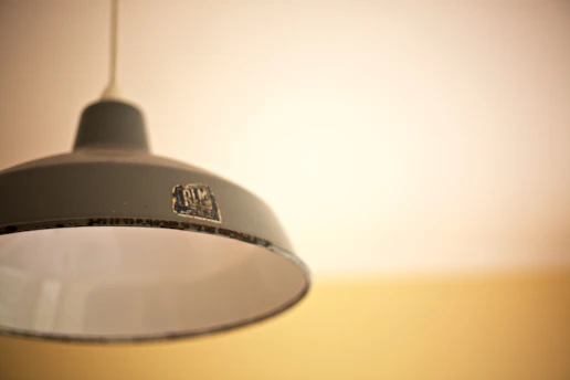 A vintage-style metallic pendant lamp hangs from the ceiling. The lamp has a label with the letters 'RLM' on it. The background features a gradient of light colors, from cream to a soft yellow hue.