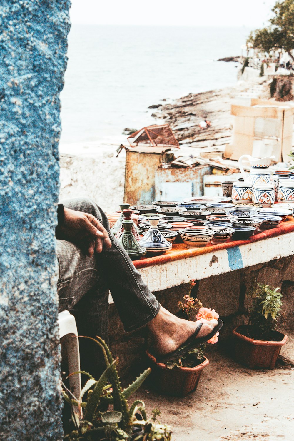 person sitting on concrete bench near assorted-color ceramic vase and bowls during daytime