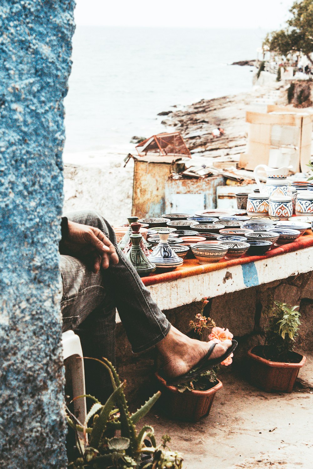 Person, die tagsüber auf einer Betonbank in der Nähe von verschiedenfarbigen Keramikvasen und Schalen sitzt
