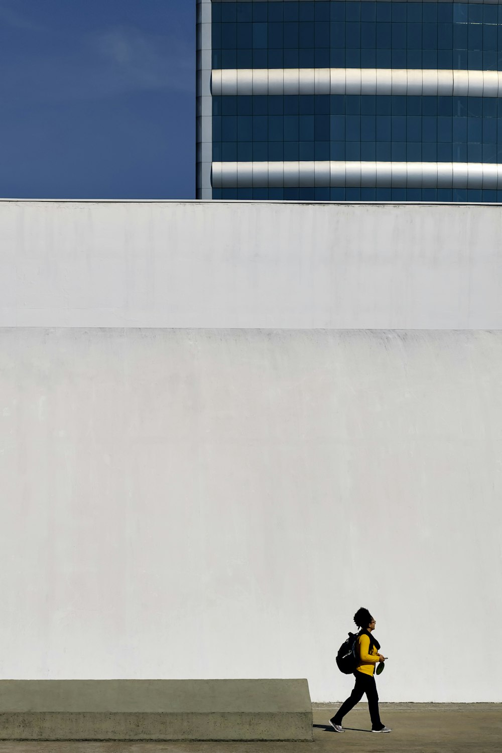 human in yellow long-sleeved T-shirt walking beside white concrete wall