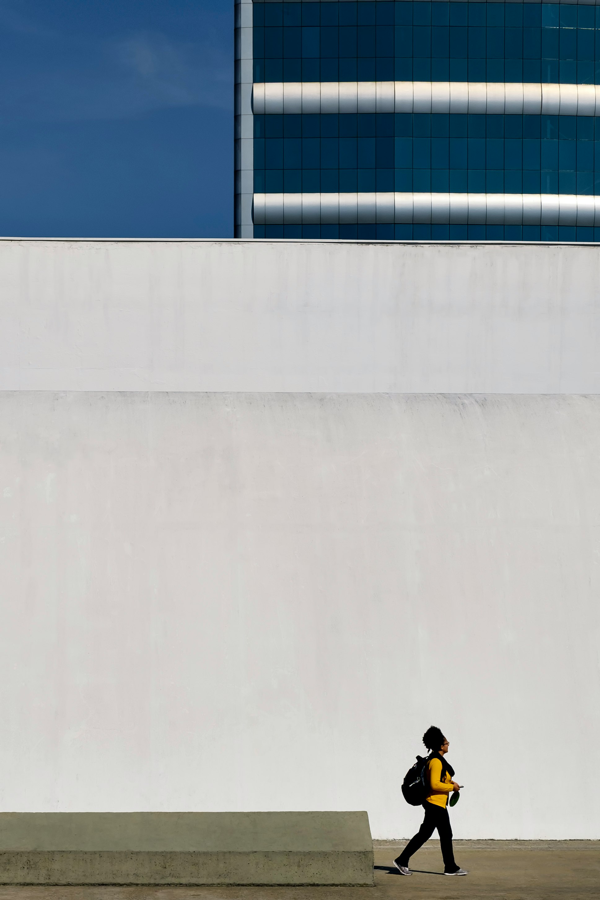 human in yellow long-sleeved T-shirt walking beside white concrete wall