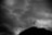 Silhouette of a person meditating in a seated position against a dramatic cloudy sky backdrop. The person appears to be levitating above a rocky terrain, adding a sense of mystery and contemplation.