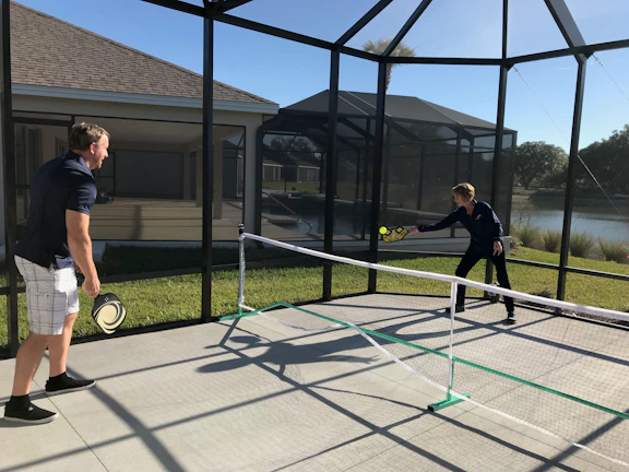 A group of friends laughing and playing pickleball on a sunny outdoor court.