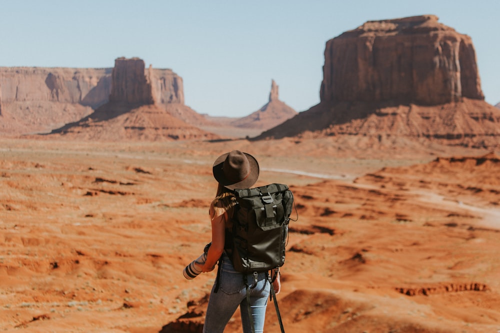 woman with black backpack standing on brown dessert