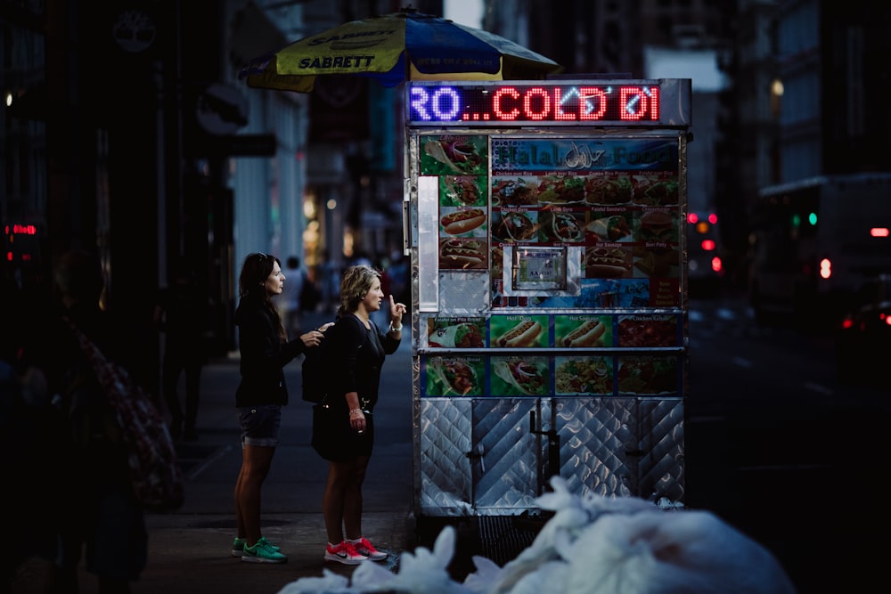 Due donne che comprano cibo sulla bancarella grigia di cibo di notte