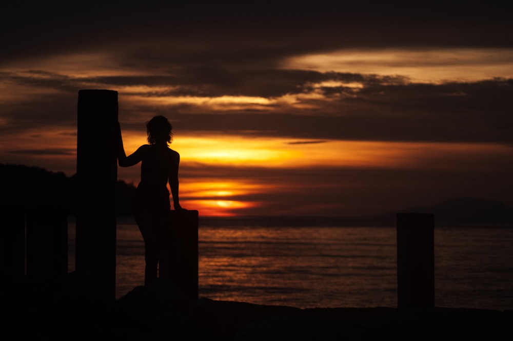 オレンジ色の夕暮れ時の埠頭の女性のシルエット