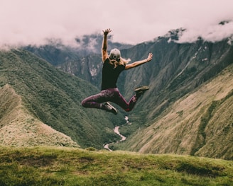 woman jumping on green mountains