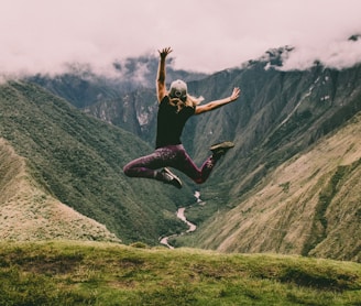 woman jumping on green mountains