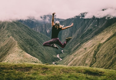 woman jumping on green mountains