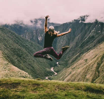 woman jumping on green mountains