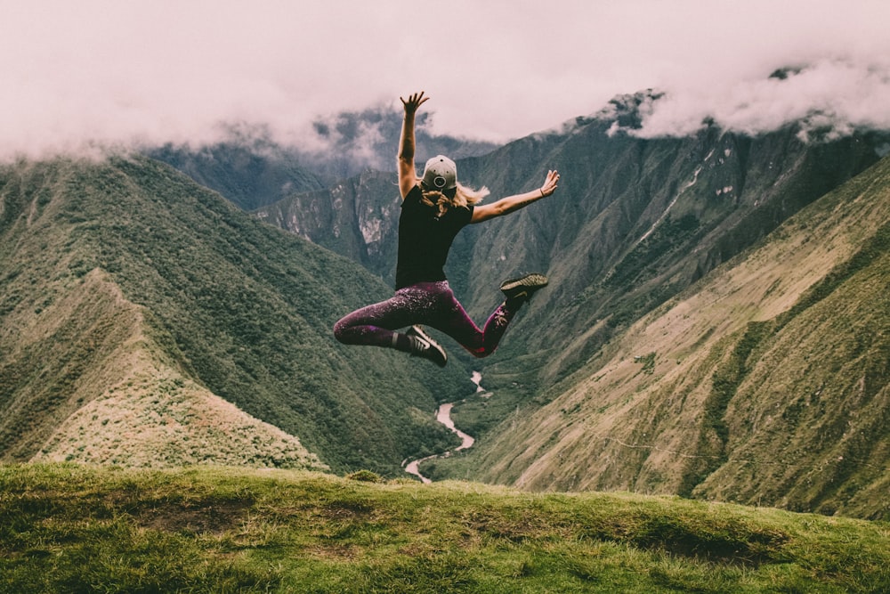 mujer saltando sobre montañas verdes
