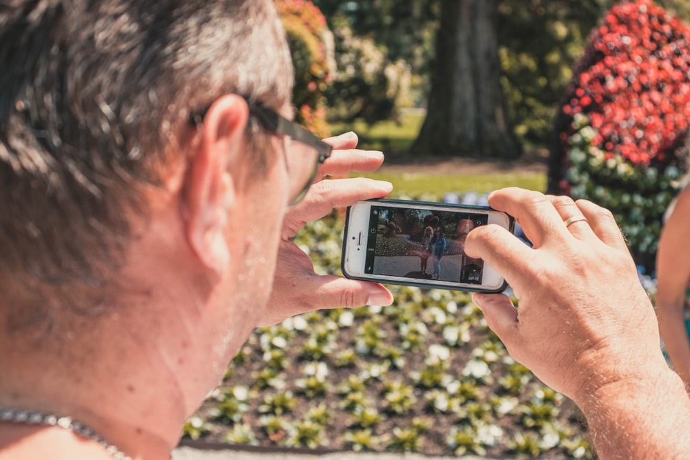 man holding white iPhone 5 taking picture of two woman standing during daytime