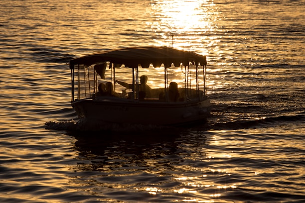 A small boat delivering fresh water to anchored yachts in a serene cove at sunset.
