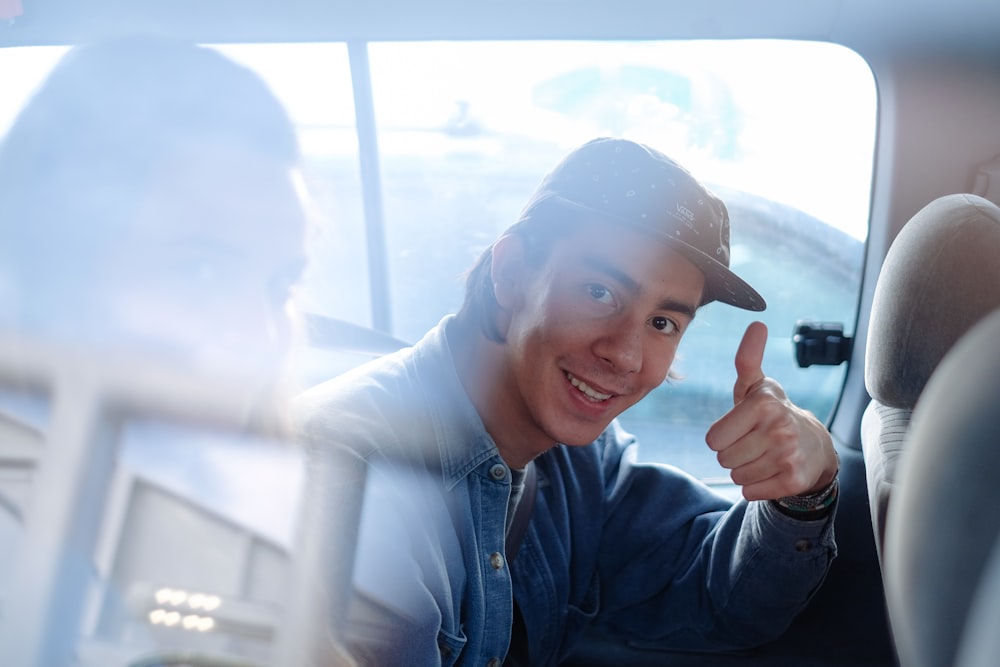 hombre sonriente dentro del vehículo haciendo pulgares hacia arriba durante el día