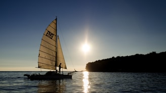 A vintage wooden sailboat gliding on calm Brazilian coastal waters at sunset.