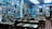 The interior of a cozy restaurant is decorated with numerous framed photographs and posters on the walls, creating a nostalgic atmosphere. Wooden tables and chairs are arranged neatly throughout the room, with patrons sitting and enjoying their meals. The lighting is soft, complementing the vibrant blue walls.