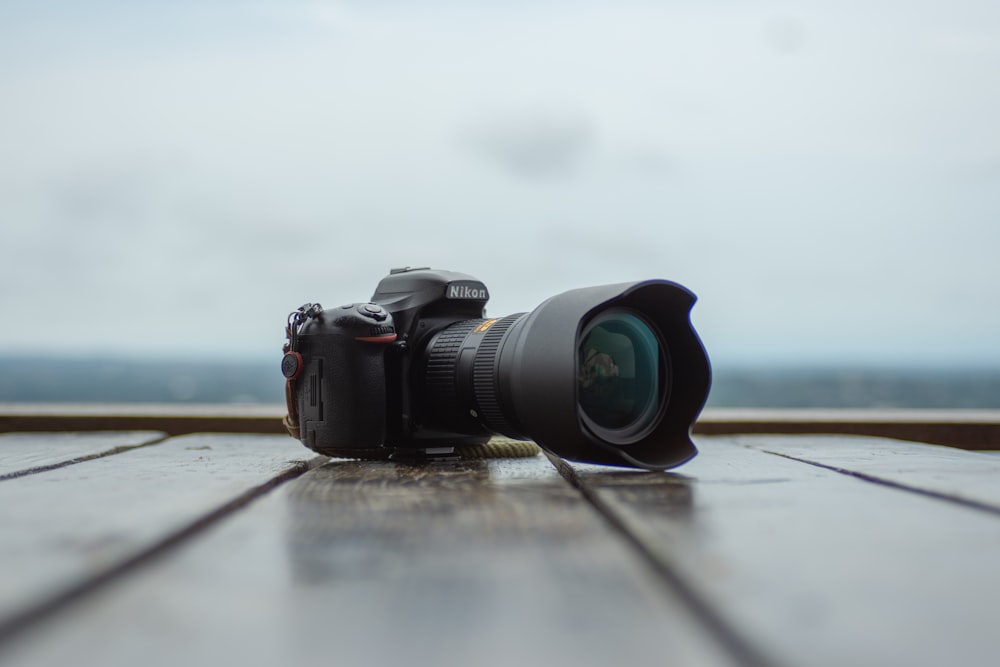 black Nikon DSLR camera on wooden plank floor shallow focus photography