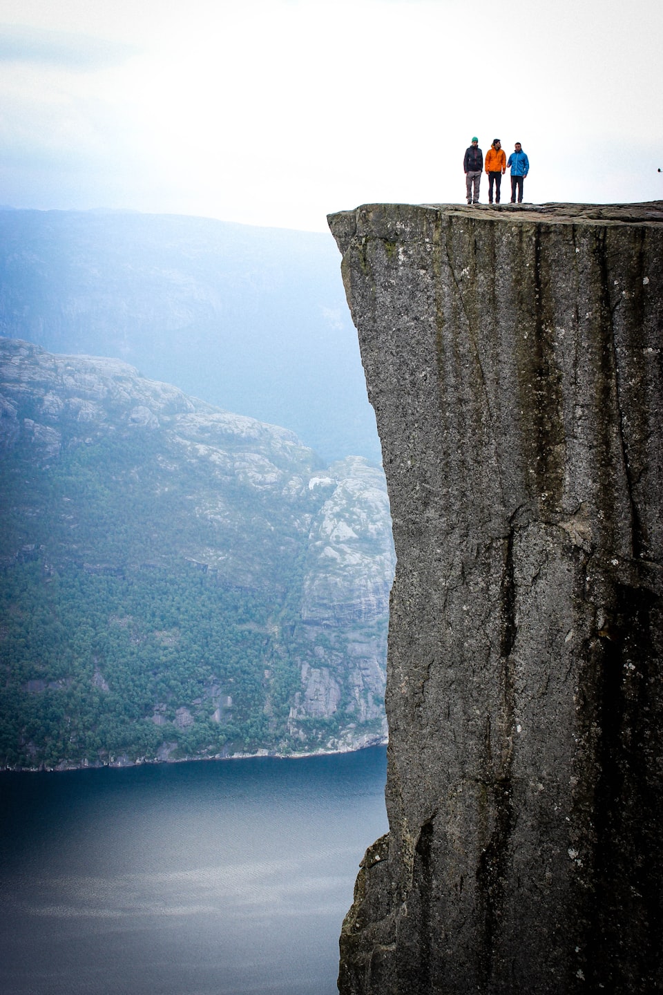 Three people standing at the top of a steep cliff.