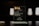 A glass award plaque etched with the text 'Dutch Interactive Awards' and other smaller inscriptions. It is placed on a black reflective surface with a blurred dark background and some softly lit cylindrical objects visible in the backdrop.