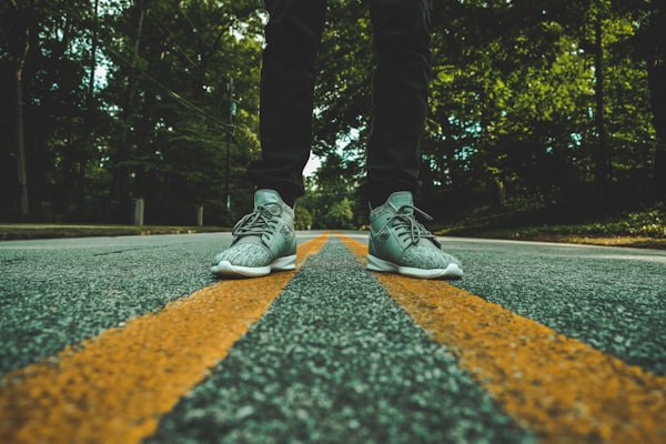 dark pants and sneakers on the middle lines of a road with trees in the background