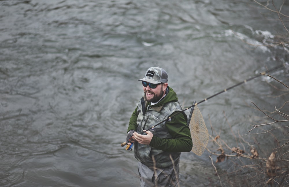 man smiling holding black fishing rod near body of water