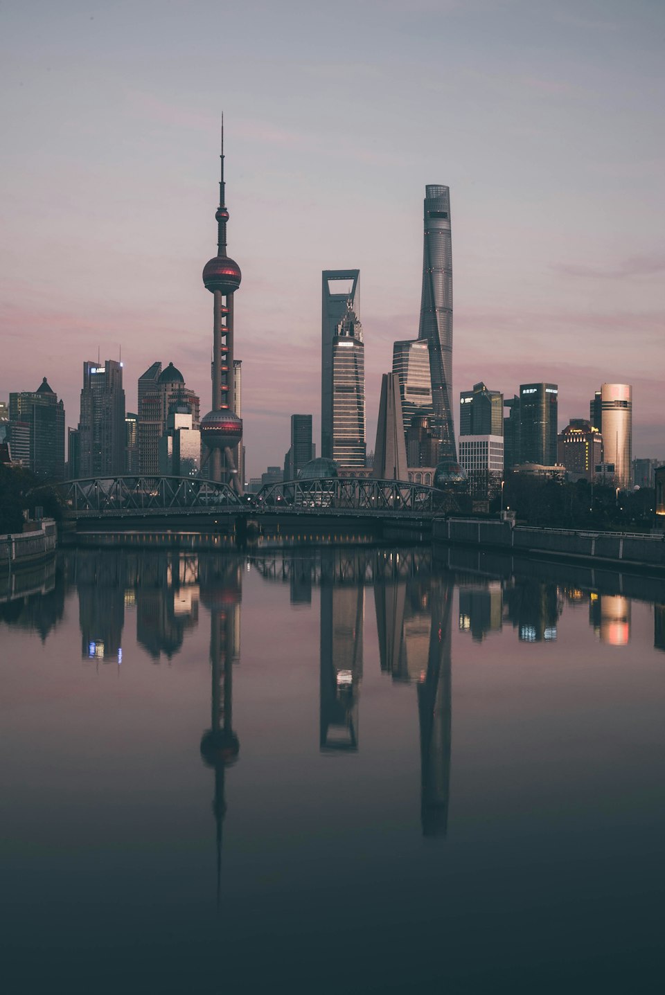 Pudong skyline with the Oriental Pearl Tower at dusk, reflected in the Huangpu River and viewed across a bridge from the Bund