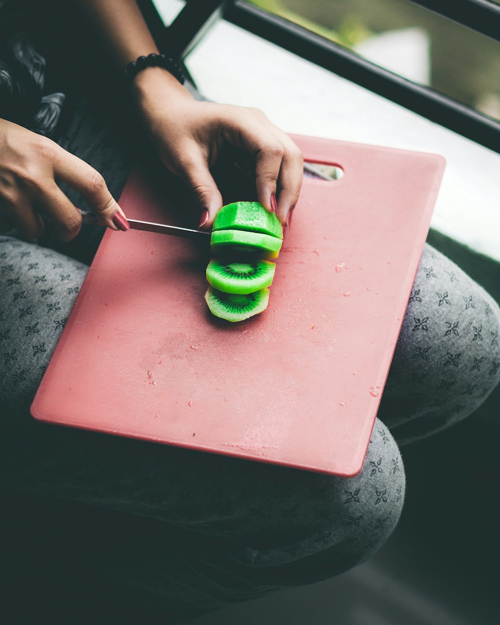 Persona cortando un kiwi verde en una tabla de cortar roja