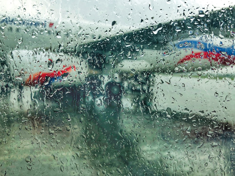 a view through a rain covered window of airplanes at an airport