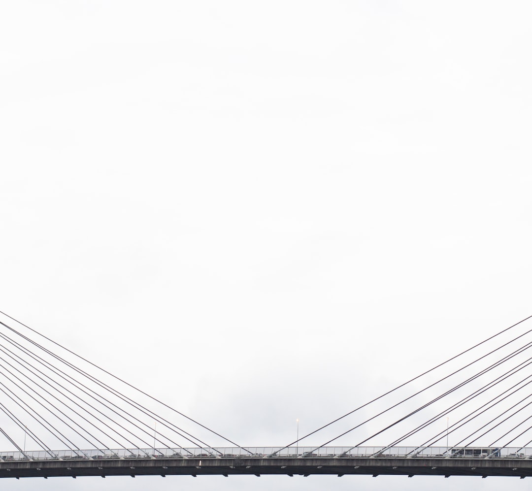 vehicles on grey suspension bridge under cloudy sky during daytime