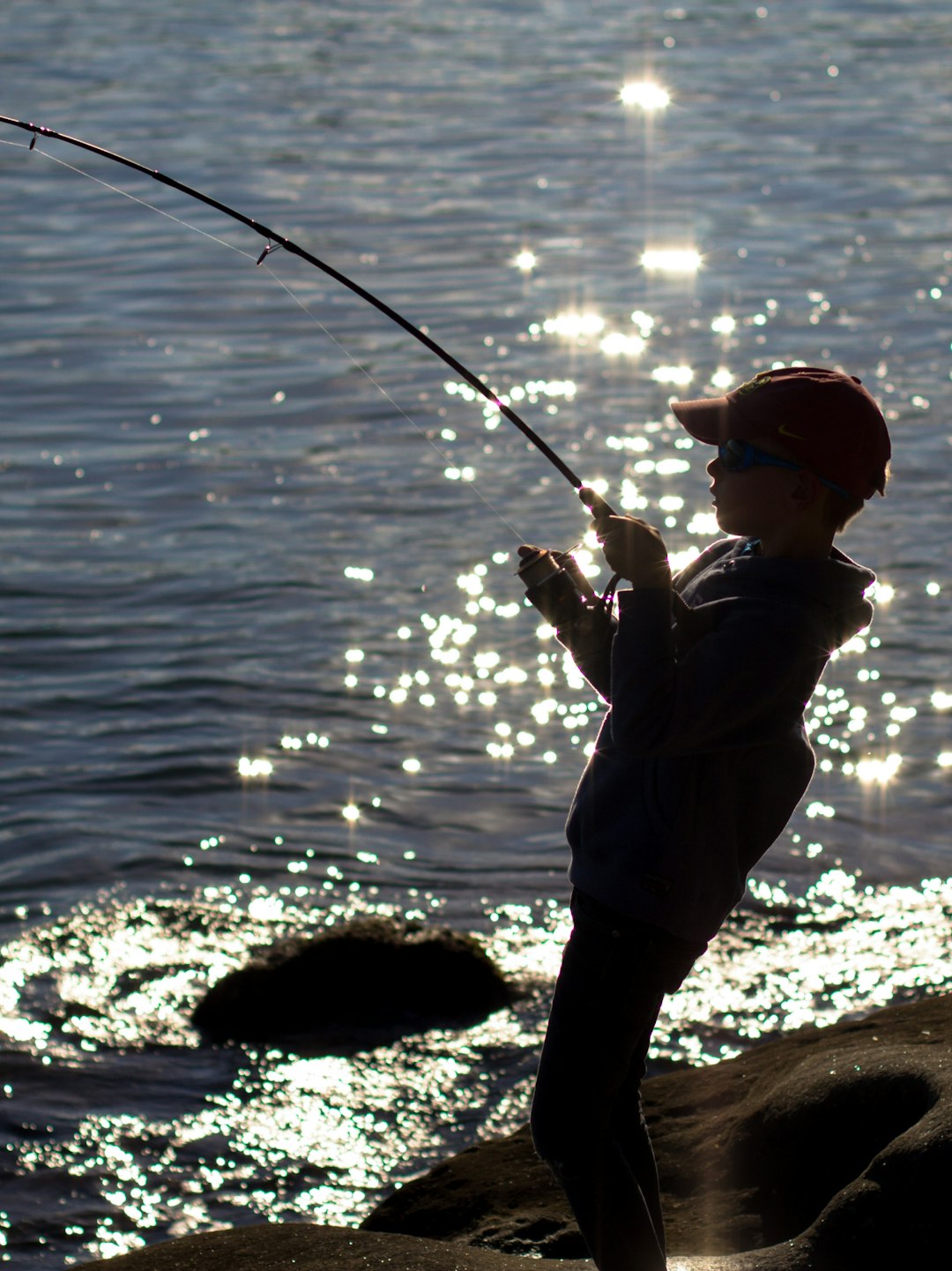 silhouette of boy fishing on shore