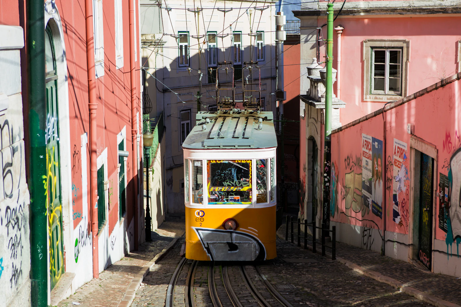 Yellow Lisbon tram passing between pink tiled walls