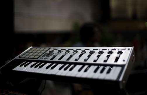 A music keyboard with various control knobs and pads is prominently featured against a blurred background. The keyboard has white and black keys along with several buttons for sound manipulation.