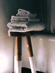 Cozy bathroom scene with neatly folded moss green and caramel colored cotton towels on a wooden shelf.