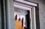 A close-up view of a broken window, with shattered glass pieces and torn paper or cardboard covering the opening. The window frame appears worn and is set against a brick wall.