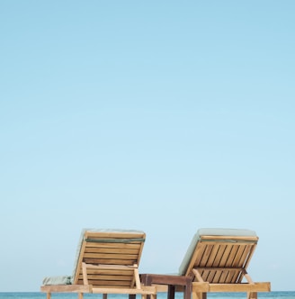 two brown wooden outdoor chaise loungers on beach