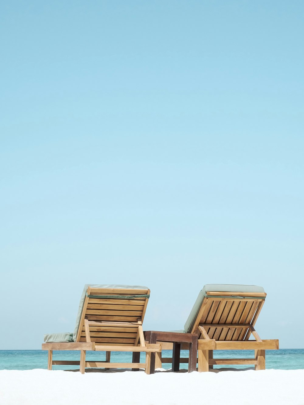 two brown wooden outdoor chaise loungers on beach