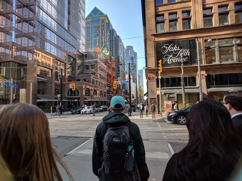 man in black hoodie wearing backpack standing in front of asphalt road