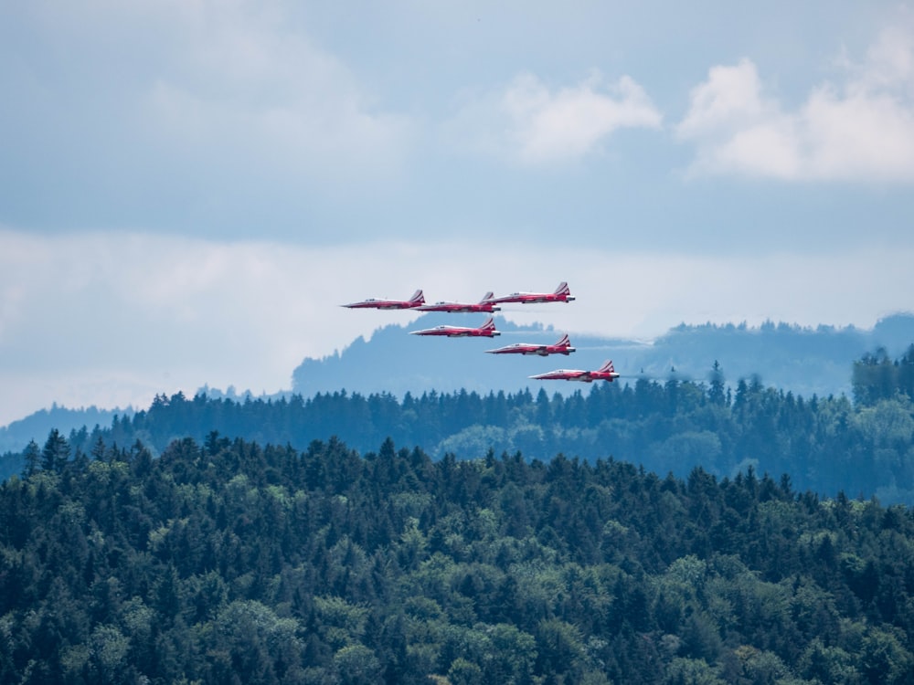 緑の山の上空を飛ぶ赤と白の飛行機