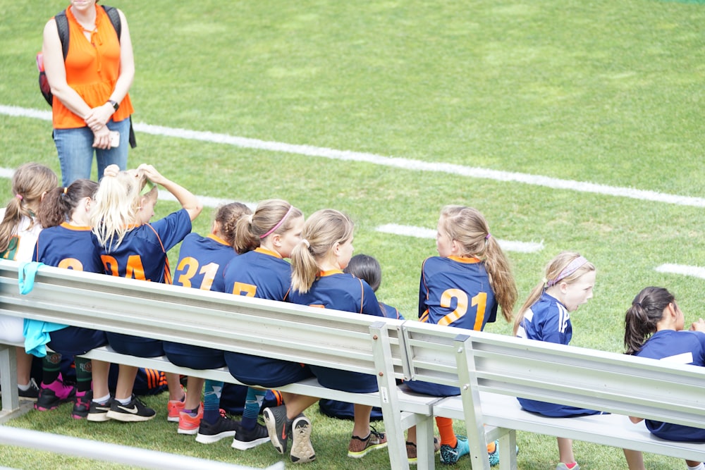 All Girl time de futebol sentado no banco branco ao lado do campo verde